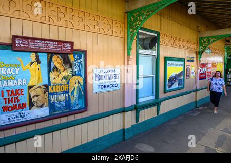 Vintage-Filmplakat und Werbeschilder am Bahnhof Horsted Keynes auf der historischen Bluebell Railway Line, East Sussex, England. Stockfoto