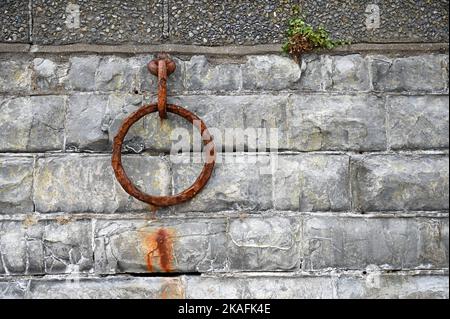 Alter rostiger Metallfestungsring an einer alten Wand. Rostige Kette aus Metall auf Steinmauer. Stockfoto