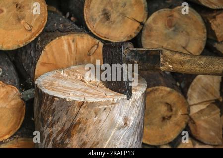 Ein Mann hackt mit einer Axt auf einem Block. Ernte von Brennholz-Vorräten zum Heizen. Eine alternative Quelle für thermische Energie anstelle von Erdgas. Stockfoto