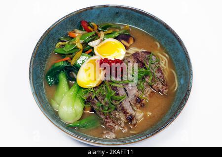 asiatische Spezialität Ramen Nudelsuppe mit Rinderstreifen, pochierten Eiern, Bok Choi und Sommergemüse in einer Schüssel Stockfoto