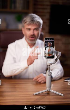 Der einflussreiche Blogger Geschäftsmann, der ein Telefon auf einem Stativ verwendet, nimmt einen Videoblog von seinem Heimbüro auf. Erfolgreiches Live-Webinar zum aktiven Chatten Stockfoto