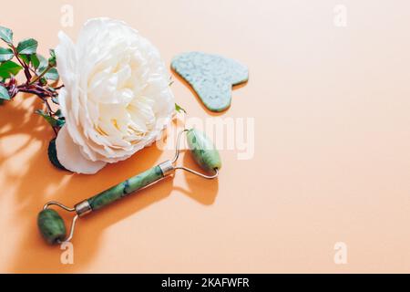 Jade Roller und Gua Sha Stein für Gesichtsmassage mit Rosenblüte. Home Beauty und Selfcare Accessoires. Anti-Aging-Werkzeug. Draufsicht. Platz Stockfoto