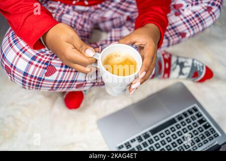 Afroamerikanische Frau mit einer Tasse heißen Kaffee auf dem Teppich am Computer Stockfoto