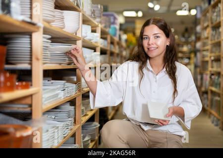 Frau wählt Teller im Geschirrladen Stockfoto