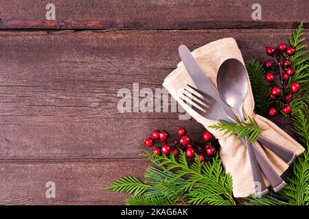 Weihnachten oder Winter Tischeinstellung Eckgrenze. Besteck und Serviette mit immergrünen Zweigen und roten Beeren. Blick von oben auf eine rustikale Holzbackgroun Stockfoto