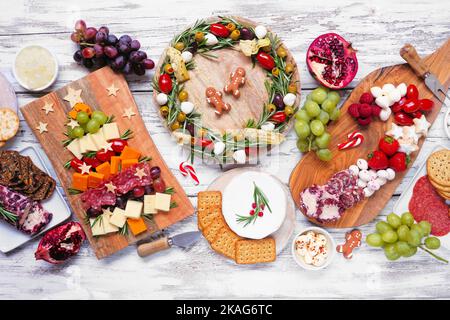 Weihnachtliche Tischszene auf weißem Holzhintergrund. Auswahl an Käse- und Fleischgerichten. Weihnachtsbaum, Kranz und Zuckerrohr arrangieren Stockfoto