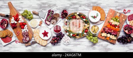 Weihnachtskarcuterie Tischszene auf einem weißen Holzbanner Hintergrund. Auswahl an Käse- und Fleischgerichten. Weihnachtsbaum, Kranz und Zuckerrohr Stockfoto