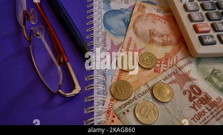 Türkische Lira, türkische Lira mit Münzen und Rechner, Stift oder Bleistift und Brille auf dem lila Notizbuchhintergrund. Stockfoto