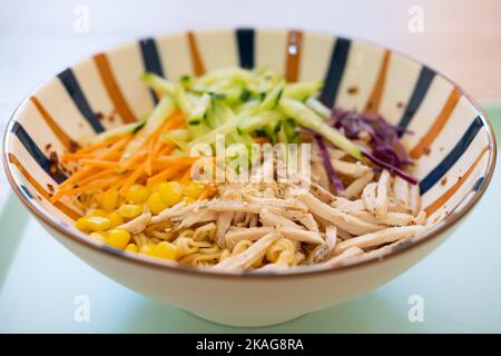 Eine Schüssel mit kalten Nudeln mit zerkleinerten Hühnchen und Gurken sowie Karotten- und Purpurkohl Stockfoto