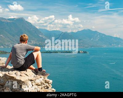 Blonde Haare Teenager mit Sport Körper ruht auf rauhen steinigen Wand über dem blauen Wasser des Gardasees, Sirmione, Manerba de Rocca, Italien. Stockfoto