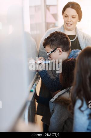 Hervorragende Ideen können von überall kommen. Ein Grundschüler, der im Klassenzimmer auf einem Whiteboard schreibt. Stockfoto