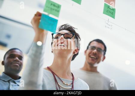 Ich glaube, ich habe etwas. Eine Gruppe von Designern, die in einem Büro mit Notizen an einer Glaswand Brainstorming. Stockfoto