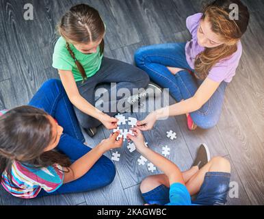 Lernen, als Team zu arbeiten. Eine Gruppe von Kindern, die ein Spiel mit Puzzles auf dem Boden halten, in einem Hochwinkel. Stockfoto