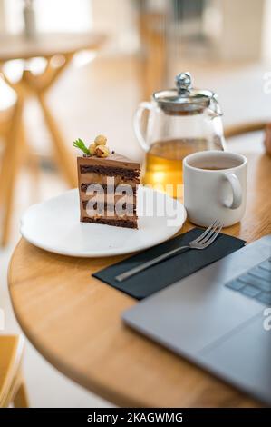 Tasse Tee und leckeren Kuchen auf Tischhintergrund mit Laptop Stockfoto