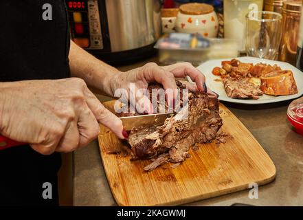 Der Koch schneidet Scheiben aus einem Stück lang gegartem Rindfleisch Stockfoto