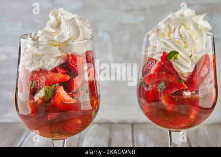Dessert mit Erdbeeren und Schlagsahne in hohen Gläsern auf Holzhintergrund Stockfoto
