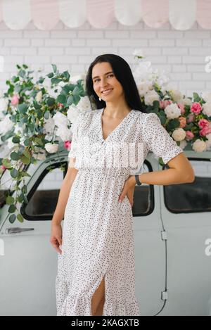 Romantische Brünette junge Frau in einem Kleid steht in der Nähe eines Retro-Autos und lächelt Stockfoto