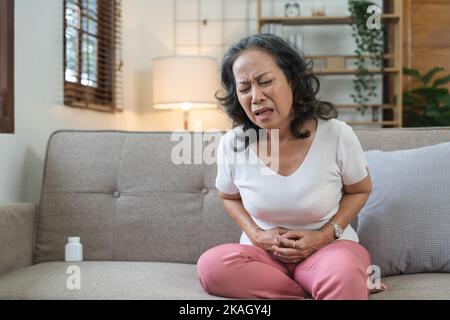 Ältere asiatische Frau mit Schmerzen durch Magenschmerzen zu Hause, ältere Frau mit Bauchschmerzen leiden Stockfoto