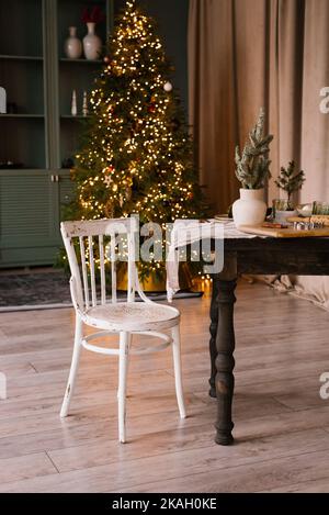 Weißer Stuhl in der Nähe eines Holztisches zu Weihnachten in einem gemütlichen und stilvollen Wohnzimmer im Haus dekoriert Stockfoto