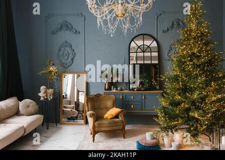 Luxuriöses Wohnzimmer in blauen Farben mit einem Weihnachtsbaum, einem Sessel, einem Sofa und einem Spiegel im klassischen Stil Stockfoto