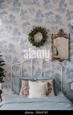 Kissen auf dem Bett, ein Weihnachtskranz an der Wand. Weihnachtliche Schlafzimmer-Innenausstattung in blauen Farben Stockfoto