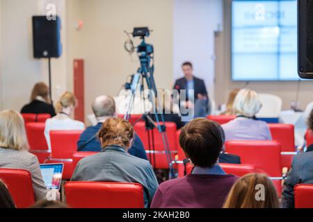 Anonyme Unternehmer, die während eines Geschäftsseminars in einem modernen Auditorium die Präsentation auf dem Bildschirm ansehen, während sie auf roten Stühlen sitzen Stockfoto