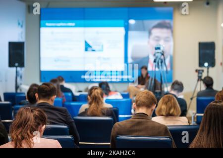 Menschen, die während eines Geschäftsseminars in einem modernen Auditorium Online-Sprecher auf dem Bildschirm hören Stockfoto