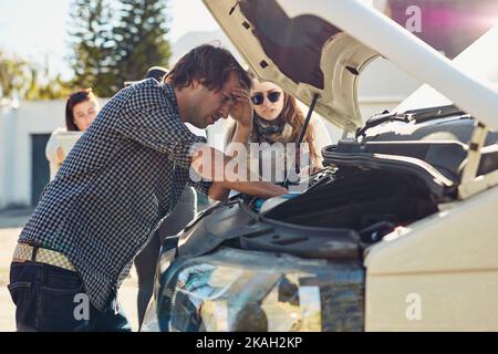 Es sieht so aus, als hätten wir Probleme mit dem Auto. Ein junger Mann, der unter der Haube eines kaputten Autos schaut. Stockfoto