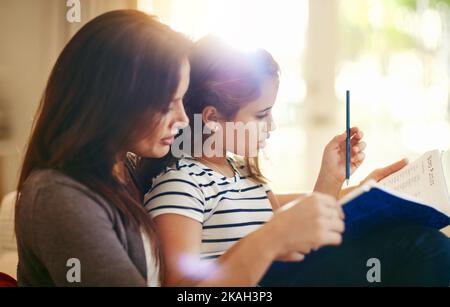 Erste Hausaufgaben vor der Spielzeit. Eine glückliche junge Mutter und Tochter genießen ihre Zeit zusammen. Stockfoto