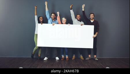 Sagen Sie es laut, sagen Sie es stolz. Studioaufnahme einer vielfältigen Gruppe von Menschen, die ein leeres Plakat in der Hand halten und vor grauem Hintergrund jubeln. Stockfoto