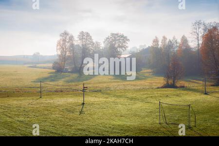 Kleiner, lokaler Fußballplatz, umgeben von Bäumen. Fußballtore und Volleyballnetz auf dem Rasen platziert. Schöner, nebliger Herbstmorgen in der Grafr Stockfoto