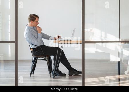 Seitenansicht des denkenden Geschäftsmannes Krypto-Trader, der an seinem Schreibtisch sitzt und den Börsenmarkt analysiert, Risiken des Handels mit Kryptowährung auf seinem Laptop. Speicherplatz kopieren Stockfoto