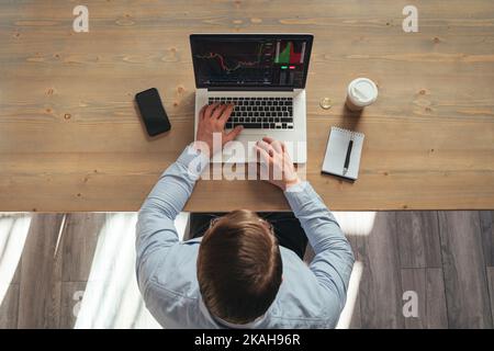 Draufsicht des Geschäftsmannes, der Kryptowährung tradet, der einen Laptop mit einer Aktienmarkt-App betrachtet, am Tisch sitzt, die Analyse von digitalen Geldcharts durchführt, der Investor Broker Indizes analysiert. Speicherplatz kopieren Stockfoto