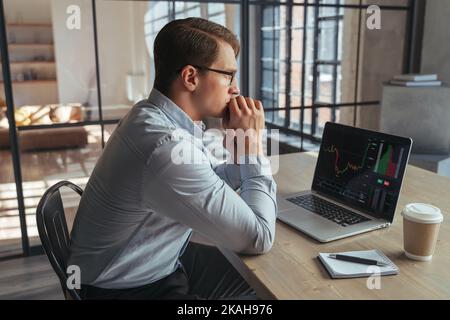 Globale Rezession und Investmenthandel. Seitenansicht des Krypto-Trader-Anlegers, der auf einen Laptop-Bildschirm mit einem Candlestick-Chart am Monitor schaut und über die globalen Risiken des Online-Aktienmarktes nachdenkt Stockfoto