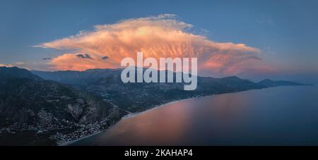 Panorama-Küstenlandschaft, abendliche Luftaufnahme der albanischen Riviera vor einem dramatischen Himmel. Strand, Berge, rosa beleuchtete Sturmwolke. Summe Stockfoto