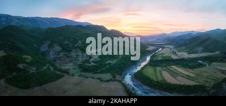 Panoramalandschaft, Luftaufnahme des Flusses Vjosë und des Tals gegen den orange-rosa Himmel. Platz für wildes Campen. Türkisfarbenes Wasser, grünes Tal, Sonne Stockfoto