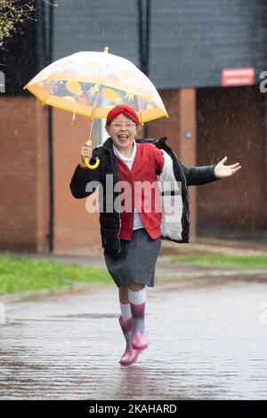 Haverhill, Suffolk, Großbritannien. 3.. November 2022. Ivy Mitchell, 7, lächelt, als sie heute Morgen im starken Regen zur Schule springt. Kredit: Headlinephoto/Alamy Live Nachrichten. Stockfoto