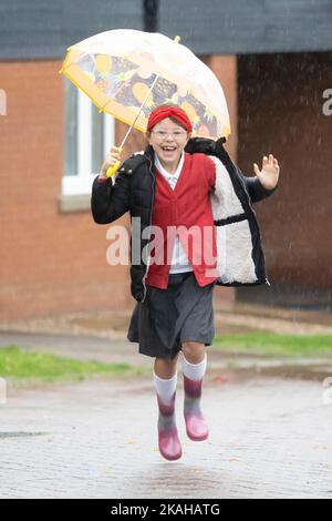 Haverhill, Suffolk, Großbritannien. 3.. November 2022. Ivy Mitchell, 7, lächelt, als sie heute Morgen im starken Regen zur Schule springt. Kredit: Headlinephoto/Alamy Live Nachrichten. Stockfoto