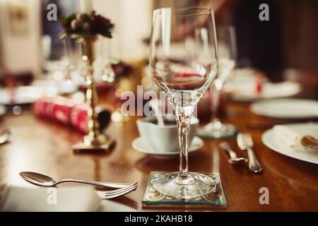 Kommen Sie Wein und essen Sie mit uns. Nahaufnahme eines Weinglases auf einem Tisch während der Weihnachtszeit. Stockfoto