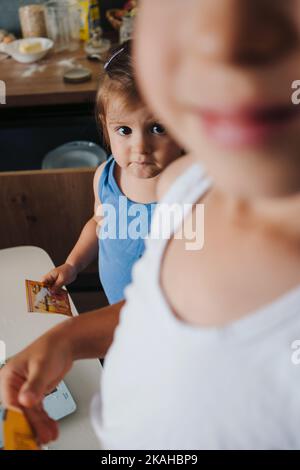 Zwei entzückende Kinder halten eine Vanilleschachtel in den Händen, die sie mit den Zutaten, die sie zum Selbstmachen benötigen, in die Schüssel gießen müssen Stockfoto