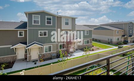 Panorama Weiße geschwollene Wolken Blick auf die Nachbarhäuser mit Rasen und Betonwegen von einer Terrasse aus. Deck eines eingezäunten Hauses mit Holzboden und Stockfoto