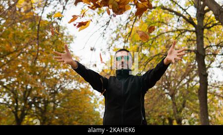 Mann, der im Park steht und Herbstblätter in die Luft wirft, Spanien Stockfoto