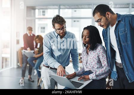 Ein Team braucht es, um ein erfolgreiches Geschäft zu führen. Eine Gruppe von Kollegen, die in einem modernen Büro gemeinsam einen Laptop benutzen. Stockfoto