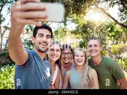 Smartphones machen das Einfangen von Momenten einfach. Eine junge Gruppe von Freunden nimmt Selfies auf, während sie draußen in der Sommersonne ein paar Drinks genießen. Stockfoto