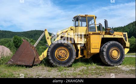 Großer alter gelber Radlader in grüner Landschaft Stockfoto