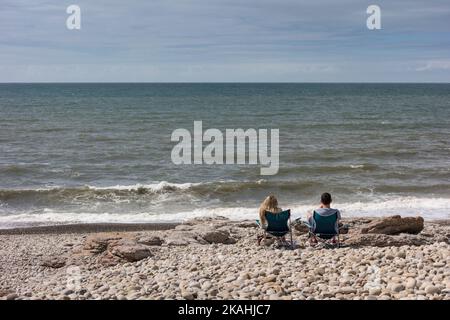 Pärchen sitzen auf Picknickstühlen und genießen den Meerblick, Ogmore by Sea, Vale of Glamorgan, Wales Stockfoto