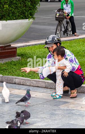 Vietnamesische Mutter und Baby, die Tauben im öffentlichen Park füttern, im Zentrum von Ho Chi Minh, Vietnam Stockfoto