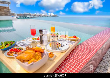 Frühstück im Swimmingpool, schwimmendes Frühstück im luxuriösen tropischen Resort. Tisch relaxen auf ruhigem Poolwasser, gesundes Frühstück und Obstteller Stockfoto