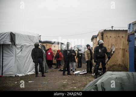 Polizeibeamte sehen als Wache aus, als das Flüchtlingslager „Dschungel“ am 01. März 2016 in Calais, Frankreich, geräumt wird. Die Behörden kehren aus weiteren Teilen des Flüchtlingslagers „Dschungel“ in Calais zurück, um Flüchtlingsunterkünfte zu räumen und versuchen, Menschen in Transportcontainer auf einem anderen Teil des Geländes zu bringen. Französische Abbruchteams begannen gestern mit dem Abbau von Hütten. Es wird erwartet, dass sich der Widerstand fortsetzt und die Polizei über Nacht Tränengas auf Migranten abfeuerte, die Steine warfen. Ein Gerichtsurteil am Donnerstag billigte einen Plan der französischen Regierung, einen Teil des Geländes zu räumen. Die Behörden sagen, dass etwa 1.000 Migranten betroffen sein sollen Stockfoto