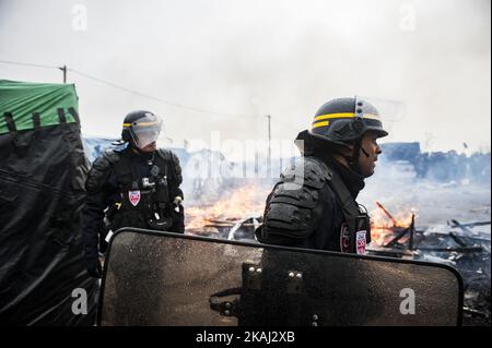 Die Polizei sicherte das Gebiet um das Feuer, nachdem sie lange Minuten auf die Zerstörung des südlichen Teils des Dschungels gewartet hatte. In Calais, Frankreich, am 1. März 2016. Beamte gehen Berichten zufolge Tür-zu-Tür im „Dschungel“-Migrantenlager in Calais, um die Menschen zu überzeugen, den Standort zu verlassen und als Asylbewerber nach Frankreich umgesiedelt zu werden. NGOs und Aktivisten sollen ebenfalls zur Verfügung stehen, um ein gerichtliches Gegenargument zu liefern. Die französischen Abbruchteams begannen Anfang dieser Woche mit dem Abbau von Hütten, aber dies wurde mit Widerstand getroffen, da die Bereitschaftspolizei gezwungen wurde, Tränengas auf Migranten zu feuern, die Steine warfen Stockfoto